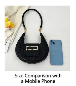 Mini black crescent handbag with crocodile pattern shown next to a smartphone for scale