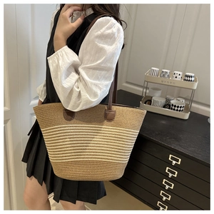 Detail of woven straw tote bag with brown leather straps and striped texture