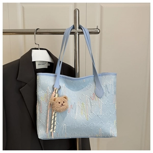 Détail d'un sac cabas matelassé bleu clair avec broderie ondulée et pendentif ours