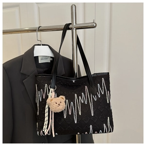 Détail du sac cabas noir avec broderie ondulée et pendentif ours en peluche marron
