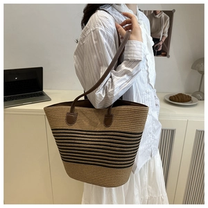 Detail of hand-woven straw bucket bag featuring black stripes and brown leather strap