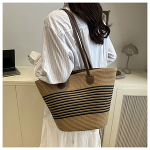 Straw tote bag with black stripes and brown leather straps shown on model's shoulder
