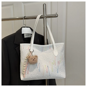 Détail du sac cabas blanc texturé avec broderie colorée et petit pendentif d'ours brun