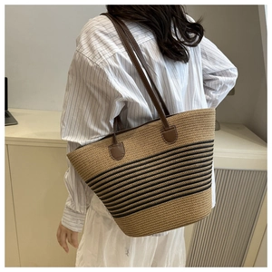 Detail of handwoven straw tote bag featuring black stripes and brown leather handles