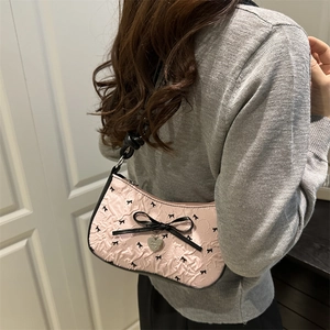 Sac sous le bras rose avec texture gaufrée et nœuds noirs porté par un mannequin en intérieur