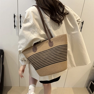Handwoven straw tote bag with blue striped bottom and leather handles for summer travel