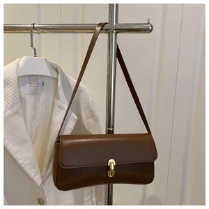 Close-up of brown leather underarm bag featuring a prominent gold oval metal clasp