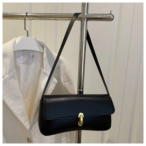 Detail of minimalist black leather shoulder bag with polished gold oval metal lock