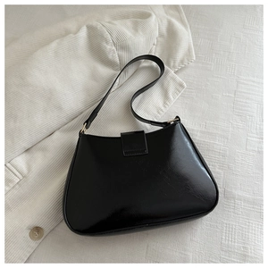 Flat lay of a black glossy faux leather shoulder bag with gold hardware on white fabric