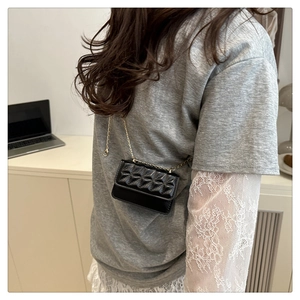 Detail of a black quilted mini crossbody bag with golden chain strap on a model