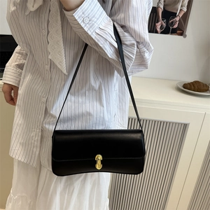 Elegant black leather baguette underarm bag with gold clasp shown on a model