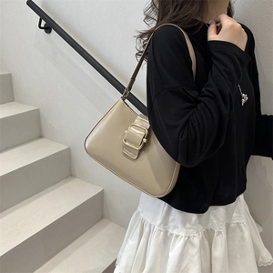 Minimalist beige underarm bag with gold buckle shown on shoulder for a retro chic look