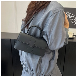 Détail d'un sac à bandoulière en cuir noir minimaliste porté par un mannequin en intérieur