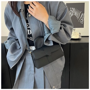 Sac à bandoulière chic en cuir noir mat porté par un mannequin au style minimaliste
