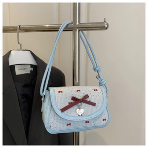 Detail of light blue crossbody bag with red bow pattern and silver heart pendant charm