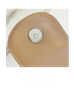 Macro view of silver magnetic clasp and litchi texture on light brown saddle bag
