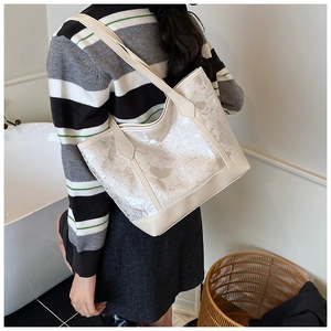 Detail of cream tote bag with translucent floral patterns and sturdy leather straps