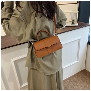 Sac à bandoulière en cuir marron porté par un mannequin avec une robe verte élégante