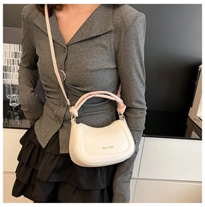 Chic beige crescent bag featuring a pink bubble handle shown on a model in a modern room