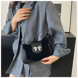 Detail of black saddle bag featuring silver bow clasp and leather metal chain strap