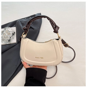 Detail of beige crescent bag with unique dark brown knotted handle and logo text