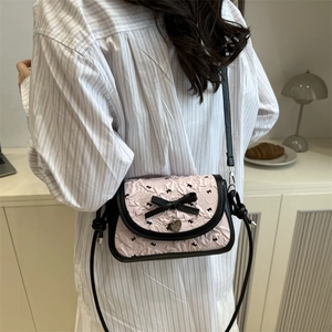 Pink embossed square crossbody bag with black bow details and heart charm on white shirt