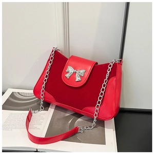 Detail of red saddle bag featuring silver metal bow and patchwork texture leather