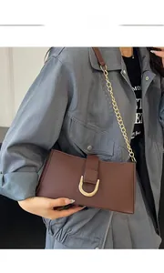 Dettaglio della borsa a tracolla in pelle marrone scuro con fibbia a U dorata su modella