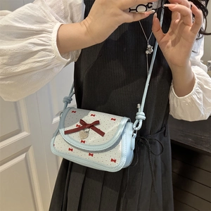 Light blue crossbody bag with red bow print and heart charm pendant shown on shoulder