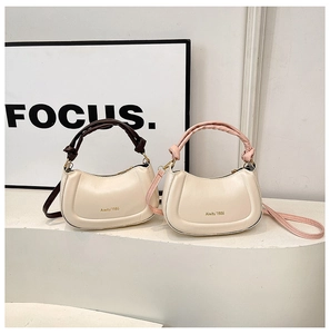 Detail view of crescent bags with woven handles in cream white faux leather and gold branding