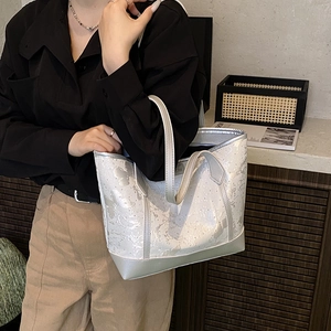 Minimalist silver tote bag with ink splash texture shown on a female model shoulder