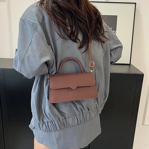 Sac bandoulière en cuir mat marron avec poignée supérieure présenté sur un modèle
