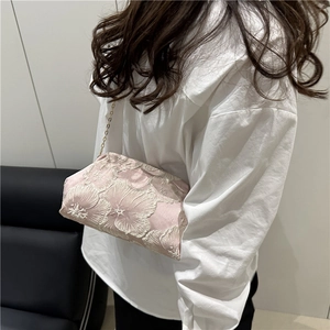 Pink satin bucket bag with white floral embroidery and gold chain strap worn by a model