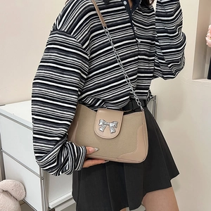 Minimalist beige suede saddle bag with silver bow buckle worn by a model in casual style