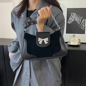 Minimalist black saddle bag with silver bow buckle and chain strap shown in a modern interior