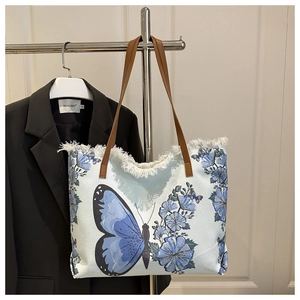 Detail of blue canvas tote featuring butterfly embroidery and boho tassel fringe edges