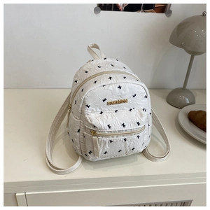 Close-up of white quilted mini backpack featuring black dog prints and gold metal logo