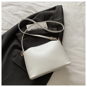 Détail d'un sac shell en cuir blanc avec boucle en métal doré sur un blazer noir