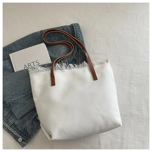 Detailed close-up of a white canvas tote bag featuring frayed edges and brown leather handles