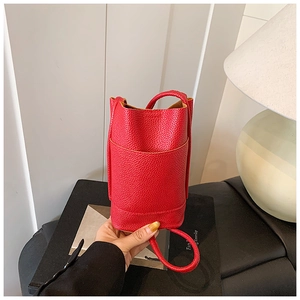 Dettaglio della piccola borsa a secchiello rossa in pelle con trama a litchi e tracolla