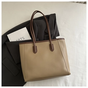 Detailed top view of a minimalist khaki tote bag with contrast brown trim on a textured surface