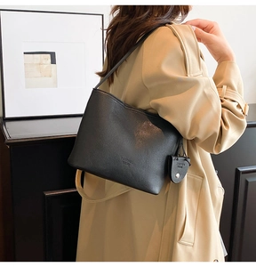 Detail of black pebbled leather bucket bag with magnetic clasp and branded logo pendant