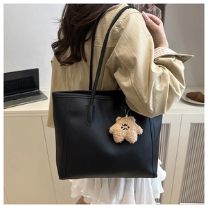 Side view of a black matte leather tote bag worn by a model with a brown plush bear charm