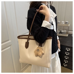 Detail of a large cream tote bag with brown straps and cute bear pendant on a model