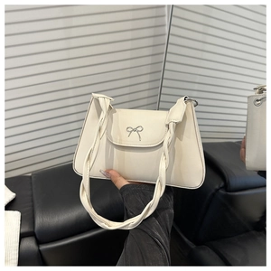 Dettaglio di una borsa a tracolla in pelle bianco crema con fiocco in metallo e manico a treccia