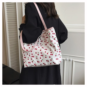 Détail d'un grand sac cabas blanc à motif cerises avec anses roses porté par un mannequin