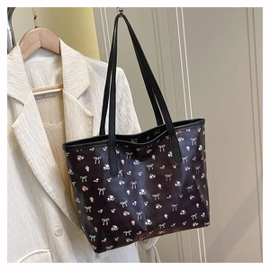 Détail d'un sac cabas noir avec motifs floraux roses et nœuds blancs sur un crochet