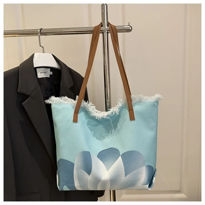 Detail of blue canvas tote bag featuring floral print, fringe edges and brown handles
