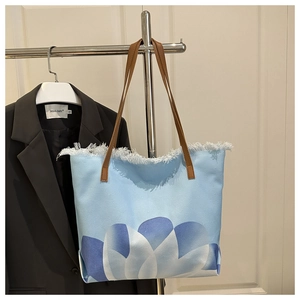 Detail of light blue canvas tote bag featuring white fringe trim and blue floral print