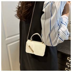Detail of white mini crossbody bag with glossy finish and elegant gold metal trim handle